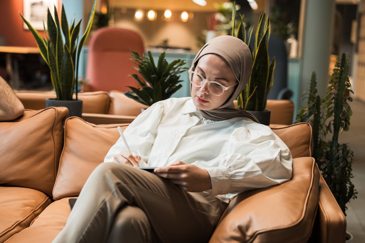 A woman in a hijab sitting on a couch with a tablet